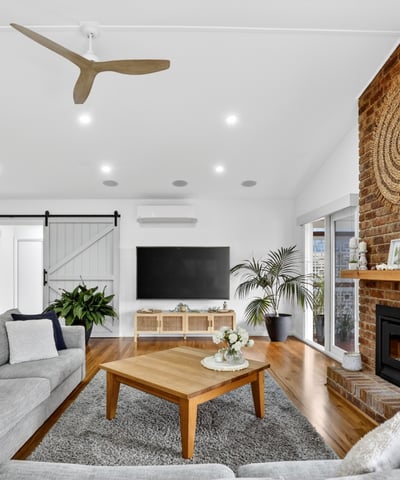 Bright and inviting living space featuring a striking brick fireplace and modern ceiling fan, perfect for gatherings.