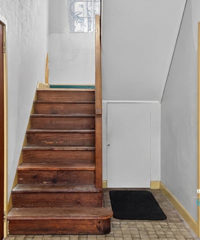 Bright entryway featuring a wooden staircase and dual access doors, perfect for welcoming guests.
