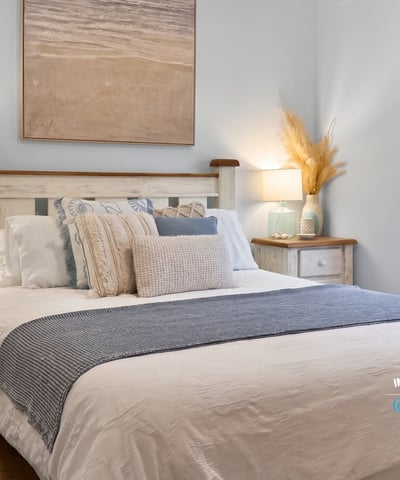 Bright and inviting bedroom features coastal decor, cozy bedding, and natural light streaming through the window.
