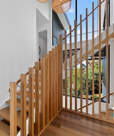Modern staircase with striking wooden accents, leading to a bright, open living space filled with natural light.
