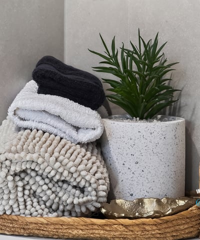 This inviting bathroom features neatly arranged towels and a contemporary plant in a chic basket.