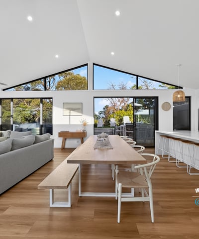 Bright and open living space seamlessly connects dining and kitchen areas, featuring large windows with natural light.