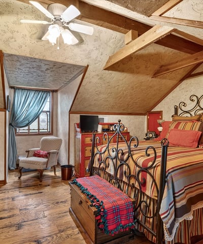 Cozy loft bedroom featuring exposed beams, a unique design, and ample natural light from large windows.