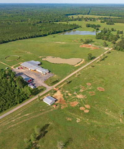 Expansive countryside property featuring vast open fields, wooded areas, and a tranquil pond, ideal for various uses.