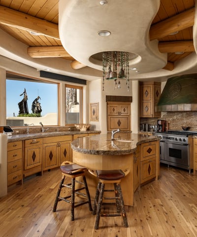 This one-of-a-kind kitchen features curved architecture, natural wood cabinetry, and luxury appliances. A center island and cozy breakfast nook offer a charming place to gather, with sweeping views right from the sink.