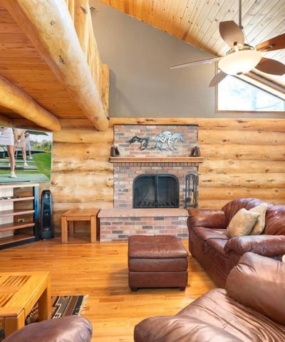 Stunning stone fireplace paired with vaulted ceilings and log construction, creating a cozy yet dramatic focal point in the main living area.