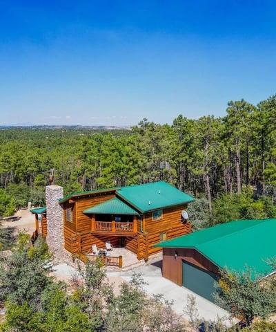Aerial view showcasing the log home, detached garage, and surrounding trees. The durable metal roofing and natural materials reflect thoughtful design in this Prescott mountain setting.