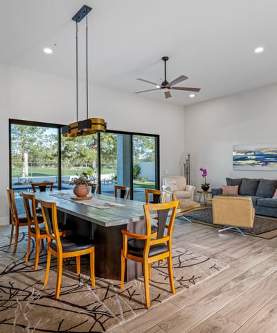 The dining space is framed by modern lighting and sliding doors, filling the room with views of the pool and golf course.
