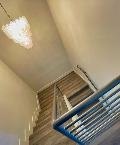 Beautifully lit staircase highlighted by a modern chandelier and open metal railing stylish and contemporary.
