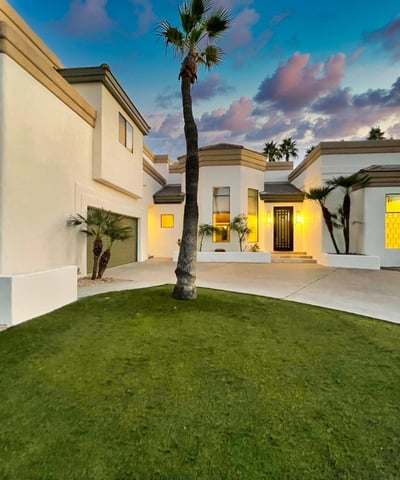The home s crisp white exterior glows against a vibrant Scottsdale sunset, surrounded by palms and a pristine front lawn.