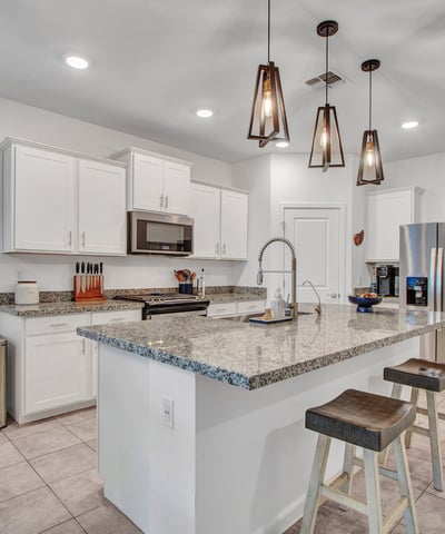 This modern kitchen highlights an oversized granite island, sleek pendant lights, stainless appliances, and energy-efficient lighting ideal for cooking and entertaining in Litchfield Park.