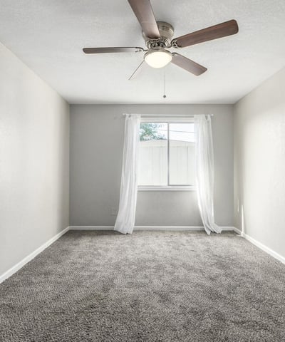 Spacious primary suite featuring plush carpeting, modern ceiling fan, and natural light perfect for rest and comfort in this Phoenix property.