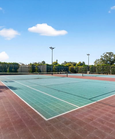 Community tennis courts surrounded by mature landscaping, offering a convenient recreational option just moments from home.