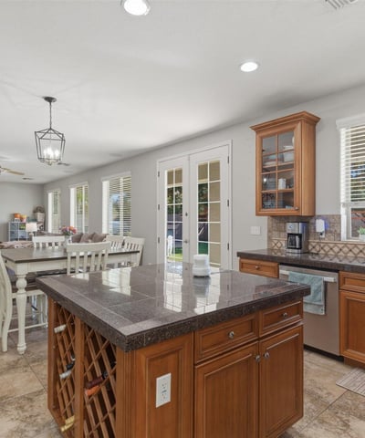 Bright kitchen with wood cabinetry, granite island, tile flooring, and large windows bringing in natural light from the backyard.