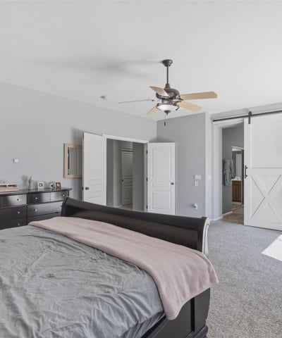 Elegant primary bedroom with barn-style sliding door access to the bathroom, spacious layout, and soft carpeting for a comfortable and stylish retreat.