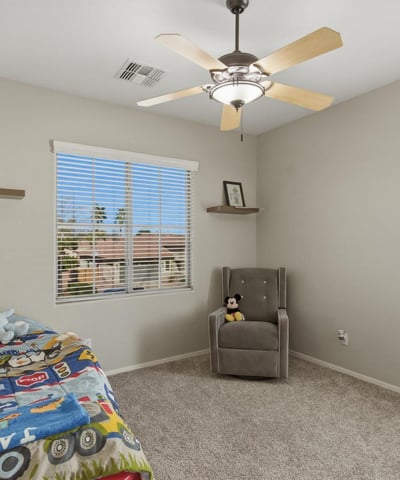Bright bedroom with plush carpet, ceiling fan, and large window providing a welcoming space for family or guests.