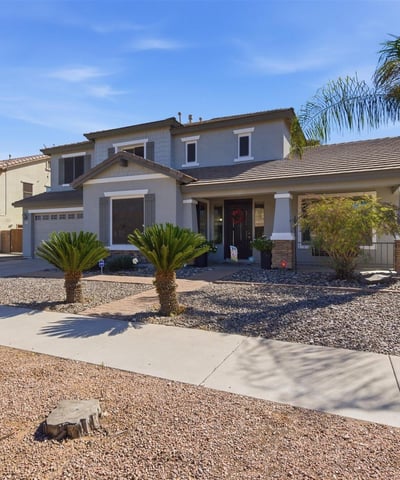 Inviting Queen Creek home exterior featuring desert landscaping, palm trees, stone accents, and a covered entry creating beautiful curb appeal.