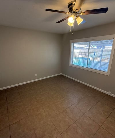Guest bedroom with tile flooring, neutral colors, and ceiling fan for comfort. Large window allows natural light while maintaining a calm and inviting atmosphere.