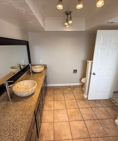 Bathroom featuring dual vessel sinks, long vanity counter, and large mirror. The design provides functionality and style within the primary suite.
