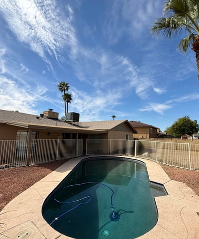 Private backyard featuring a Pebble Tec pool framed by mature palm trees and block wall fencing. The tranquil outdoor setting enhances the home s relaxing backyard atmosphere.