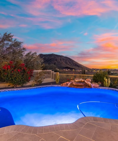 Scottsdale luxury pool illuminated at dusk with natural rock accents and sweeping mountain views, creating a serene and upscale backyard retreat.