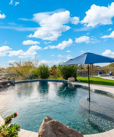 Scottsdale pool featuring built-in umbrella seating area, surrounded by pavers and landscaped yard, ideal for outdoor enjoyment.