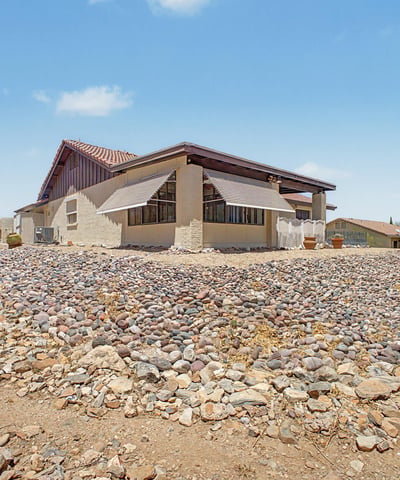 This rear exterior view highlights the home's attractive architecture, mature desert landscaping, and elevated setting. The spacious lot and low-maintenance grounds contribute to the property's appeal in Fountain Hills.