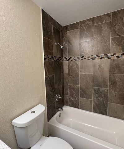 Attractive guest bathroom showcasing a stylish tile tub surround with decorative accent details and updated finishes. The refreshed design offers durability and timeless appeal.
