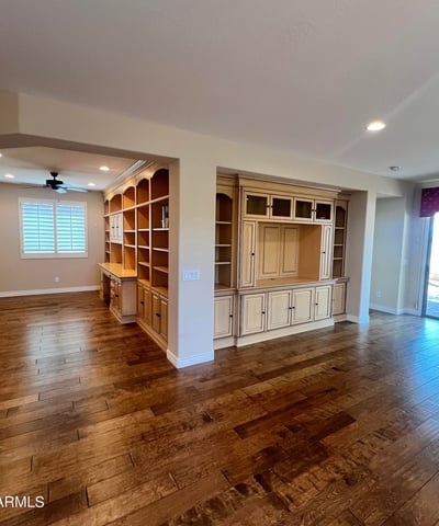 Open great room with stunning custom entertainment cabinetry, built-in office shelving, upgraded wood flooring, recessed lighting, and plantation shutters creating an elegant and highly functional living space.