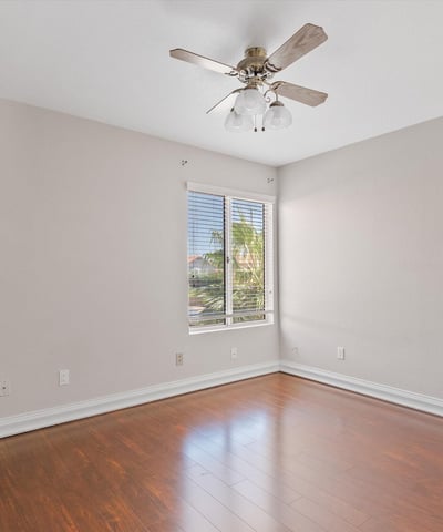 Large windows bring abundant natural light into this inviting bedroom featuring wood flooring, neutral finishes, and a ceiling fan. A comfortable space that complements this Chandler home.