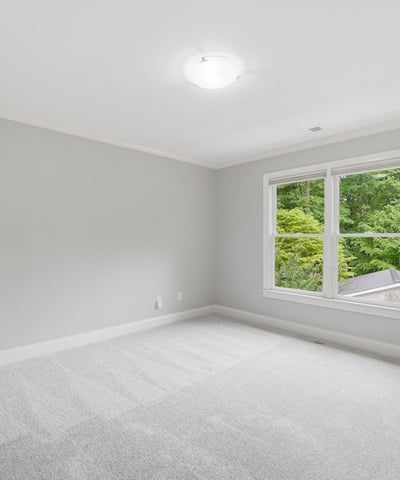 Bright, airy bedroom featuring fresh carpet, ample natural light, and a view of the lush outdoors.