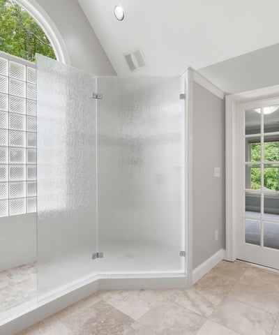 Bright and airy bathroom features a spacious glass shower and double French doors for added luxury.
