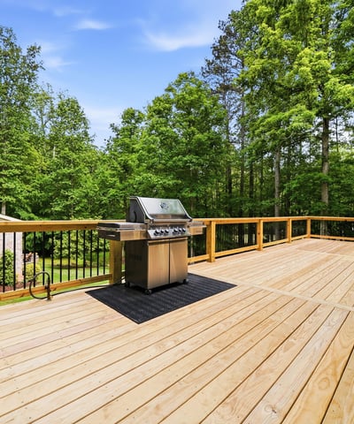 Spacious outdoor deck featuring a built-in grill, perfect for gatherings amidst lush greenery.