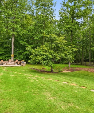 Spacious backyard with a cozy fire pit surrounded by lush greenery, perfect for gatherings and relaxation.