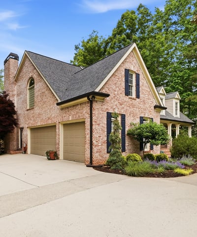 Stunning brick home with a spacious driveway, surrounded by lush landscaping and mature trees.