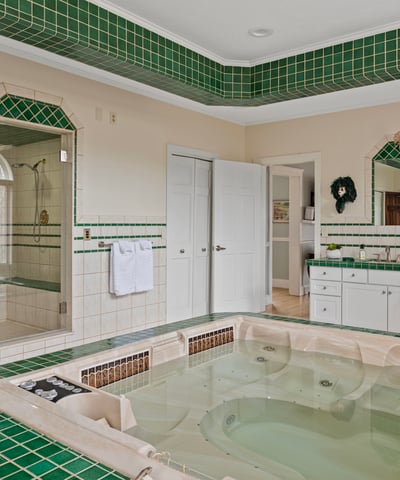 Spacious bathroom featuring a luxurious jetted tub, large walk-in shower, and distinctive green tile accents.