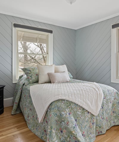 This inviting bedroom features cozy decor, ample natural light, and a tranquil view from the windows.