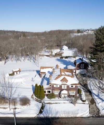 This expansive property features a beautiful home surrounded by lush trees and serene winter landscapes.