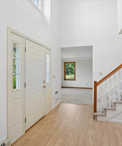 Bright and inviting entryway featuring a two-story ceiling, staircase, and views of the spacious living area.