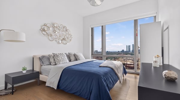 Bright bedroom featuring large windows with stunning city views and modern furnishings for comfortable living.