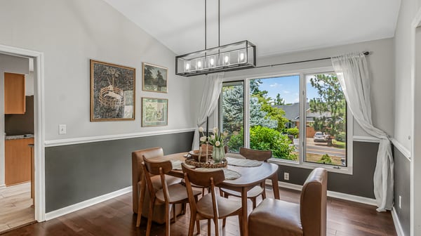 Bright dining area features large windows and a modern light fixture, perfect for gatherings and meals.