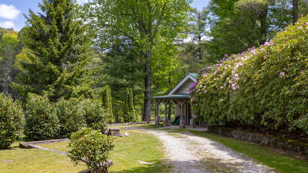 This picturesque property features lush landscaping, a winding gravel drive, and a cozy entrance nestled among the trees.