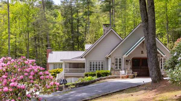 Nestled among lush greenery, this inviting home features a spacious driveway and warm outdoor gathering areas.