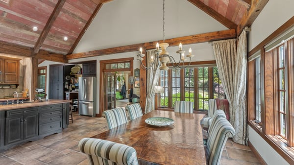 Sunlit dining area with vaulted ceilings, featuring rustic wood beams and large windows overlooking the garden.