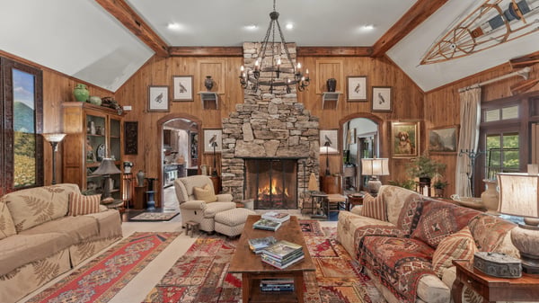 Spacious living area features a stone fireplace, wood paneling, and panoramic windows for natural light.