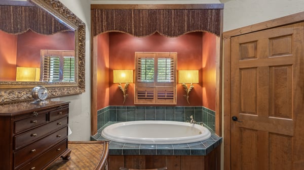 Relax in this inviting bathroom featuring a corner tub, warm lighting, and rich wooden accents.