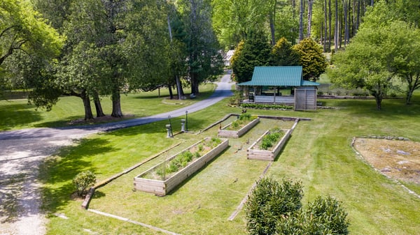 Spacious outdoor space featuring raised garden beds, a cozy gazebo, and lush greenery, ideal for gardening enthusiasts.