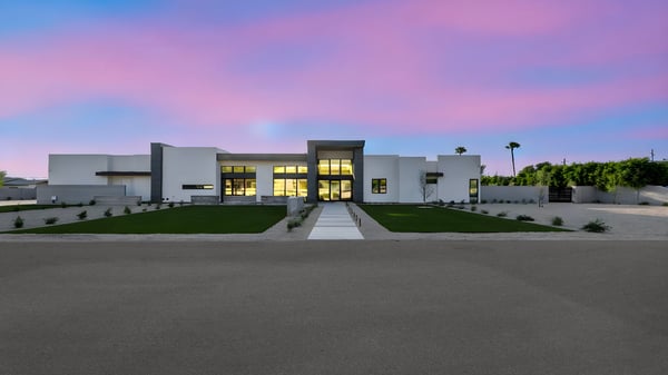 Exterior view at dusk with glowing interior lights and dramatic sky backdrop. This Paradise Valley home offers stunning evening curb appeal.