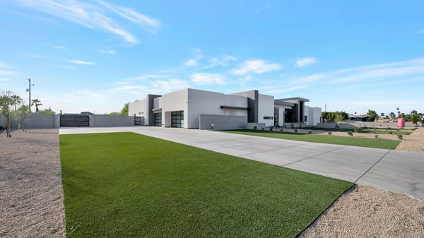 South-facing view featuring a long driveway, green lawn, and contemporary exterior. This Paradise Valley property offers a spacious lot with modern curb appeal and clean landscaping.