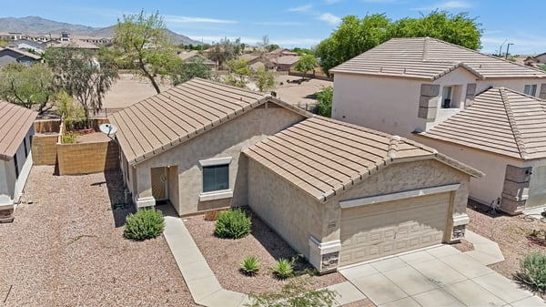 Front exterior showcases clean architectural lines, mature desert landscaping, a spacious driveway, and an attached garage. This Buckeye home offers excellent curb appeal with mountain views and open surroundings.